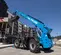 Rear angled view of a blue Genie telehandler with extended boom lifting pallets outdoors with an operator inside the cabin.